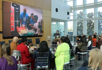 Photo from YES YOU CAN luncheon feature guests sitting and watch video about the pilot program