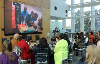 Photo from YES YOU CAN luncheon feature guests sitting and watch video about the pilot program