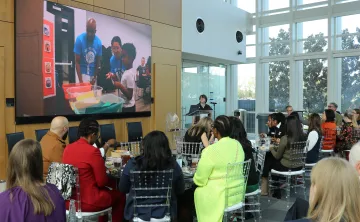Photo from YES YOU CAN luncheon feature guests sitting and watch video about the pilot program